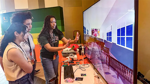 Graduate student in interactive media Ma’at Hetep explains to students Faith Jimenez, left, and Barbara Griffin how the virtual reality murals experience “Telling Overtown Stories, Saying Their Names” works. (Photo: Robert C. Jones Jr., University of Miami)